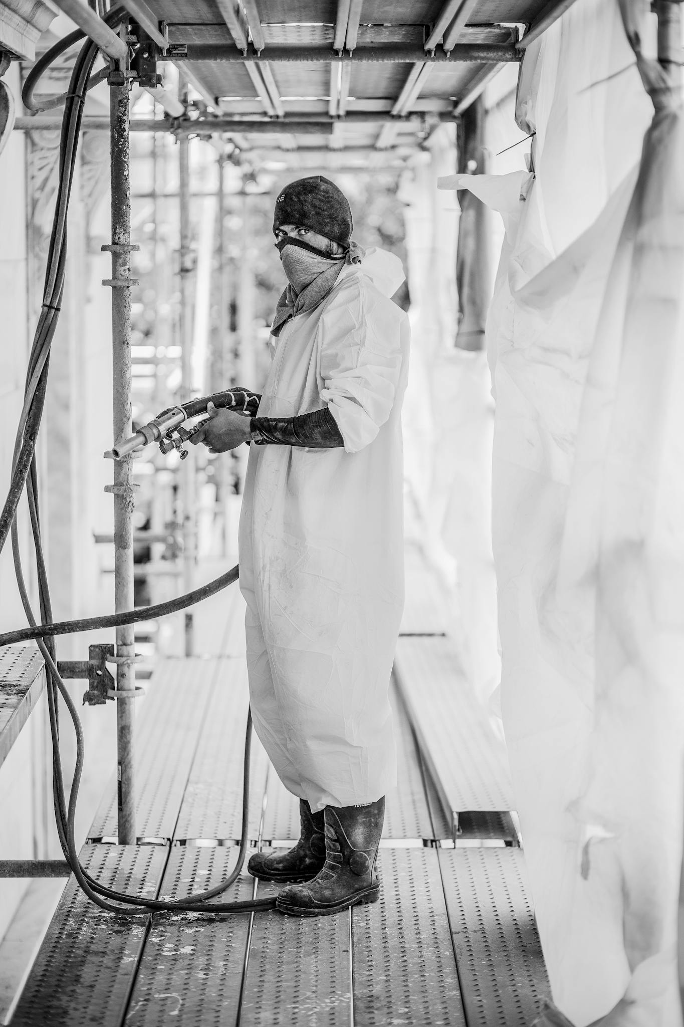 Black and white image of an industrial worker spraying in a protective suit.